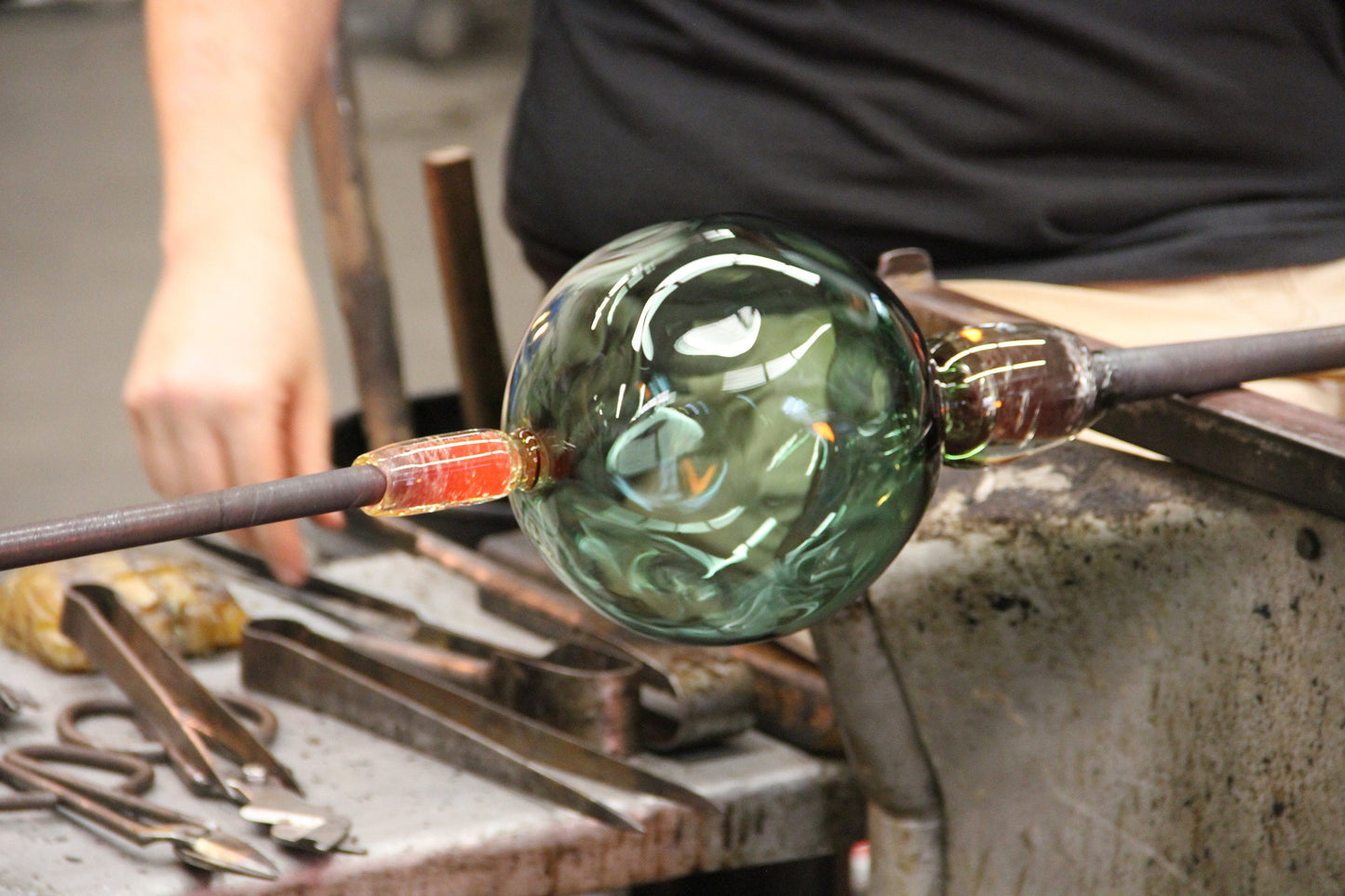 Artisan shaping a handblown glass orb for modern luminaire design, showcasing craftsmanship and unique glass texture.