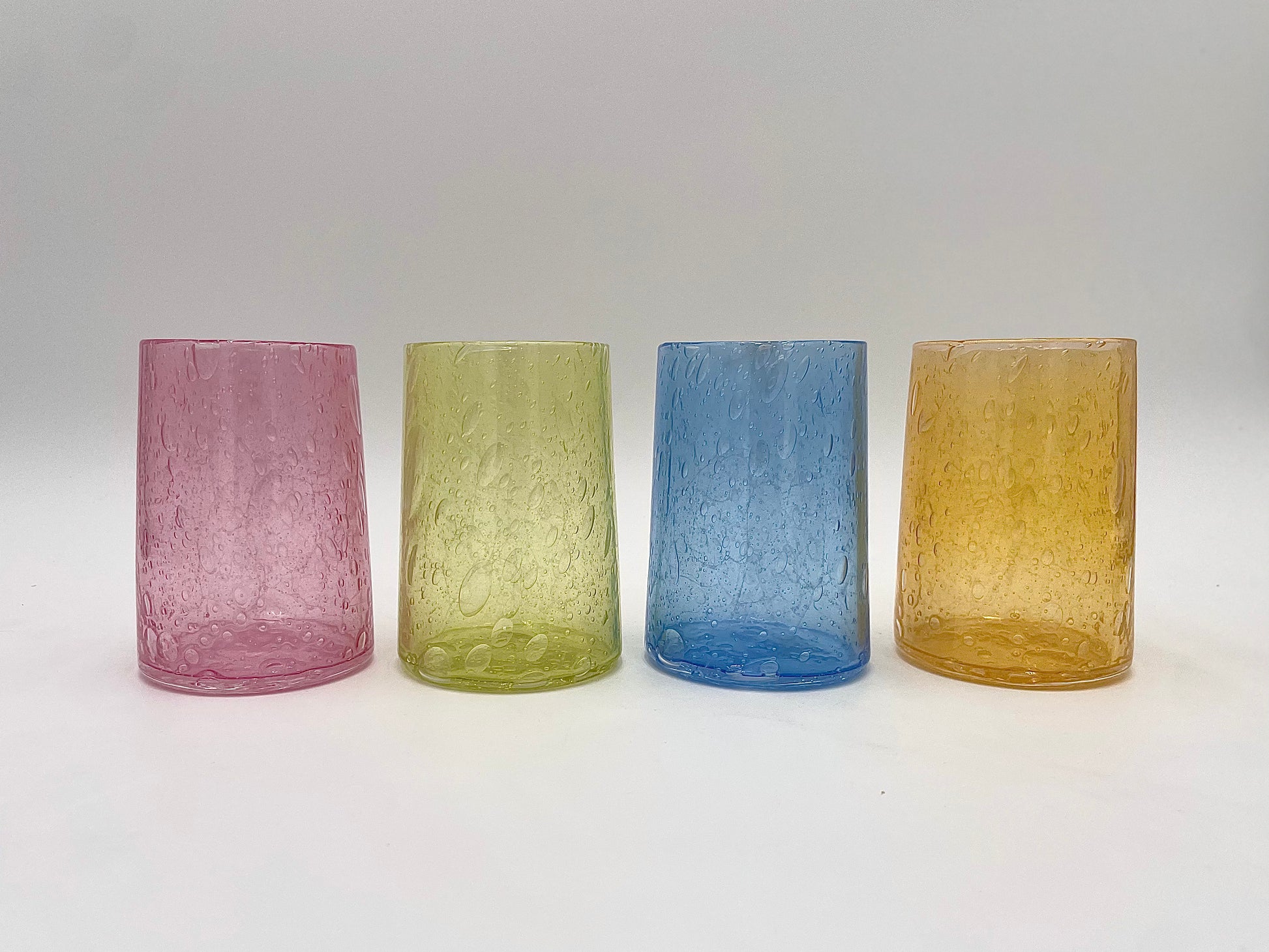 Four textured glass tumblers in pink, green, blue, and yellow on a white background
